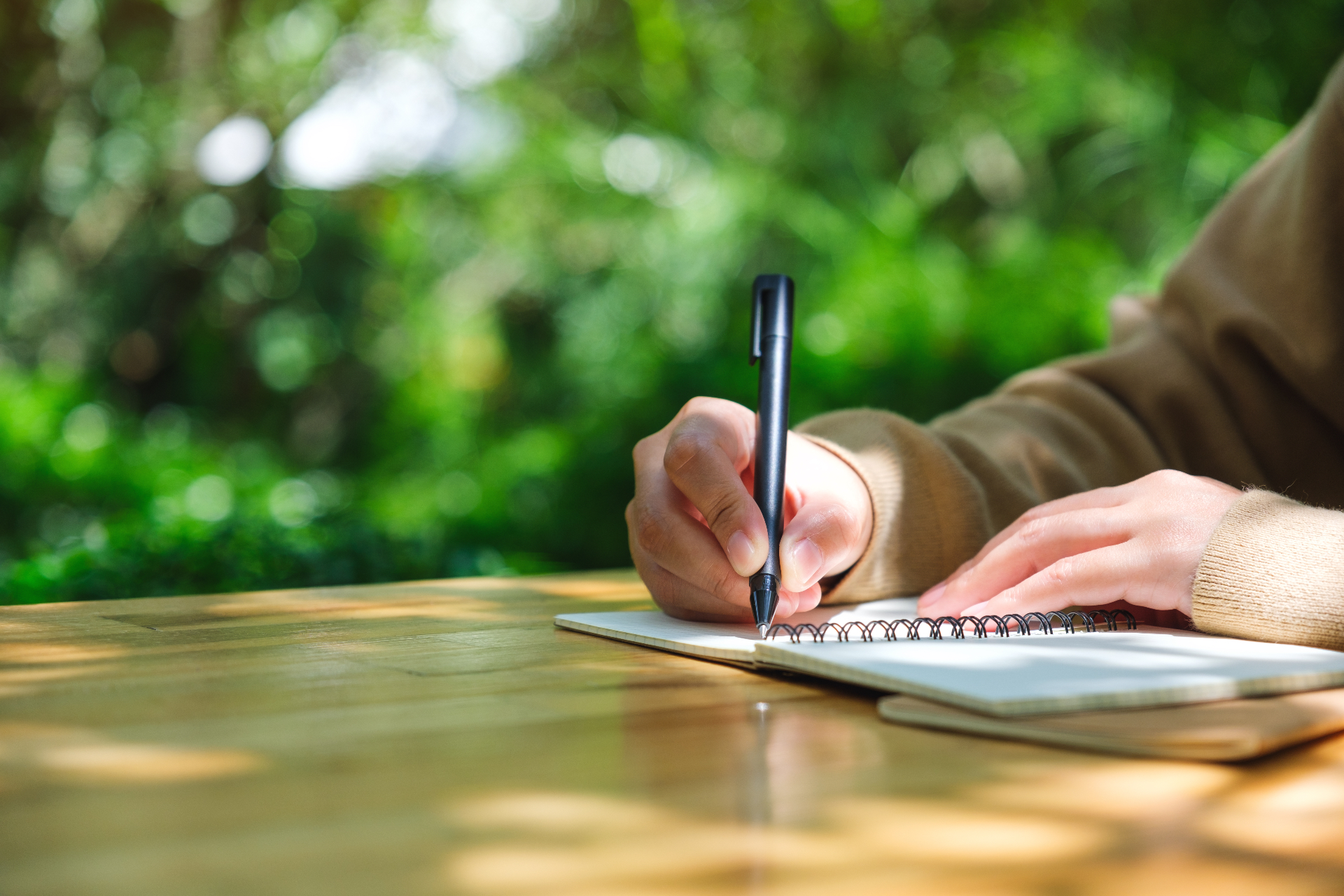 Hand schreibt mit Stift in ein Notizbuch im Freien